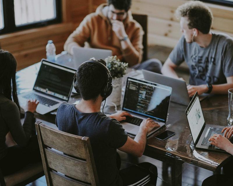 mehrere Personen sitzen mit Laptops an einem Meetingtisch