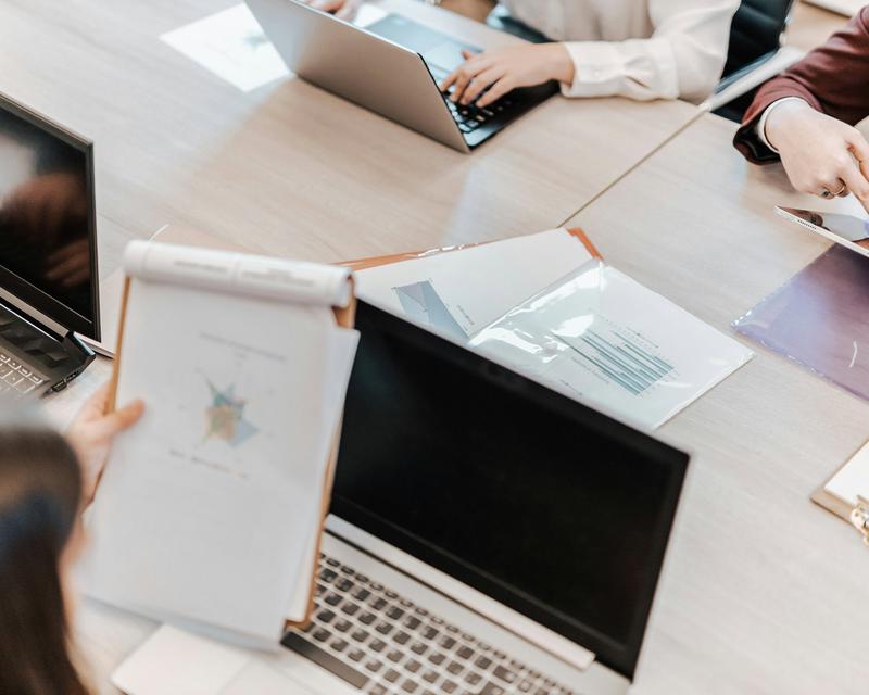 Detailaufnahme eines Meetingtisches mit einigen Personen rundum